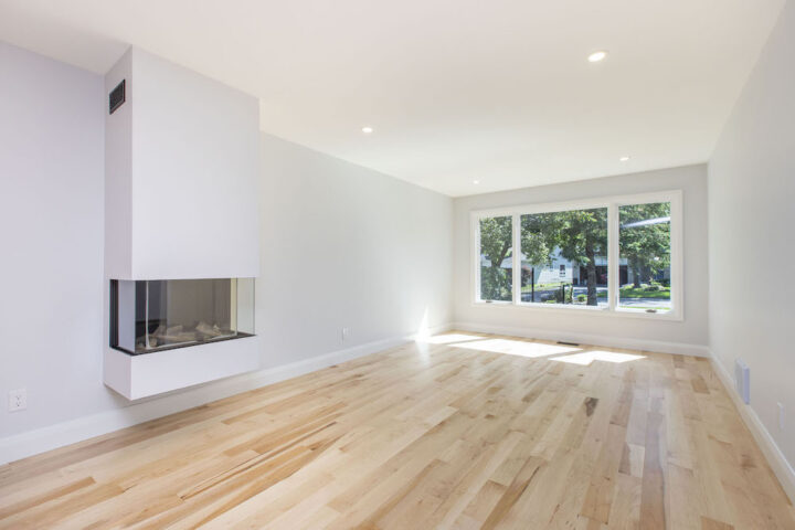 Bright living room with natural maple hardwood, a white wall-hung three-sided fireplace and a wide front window