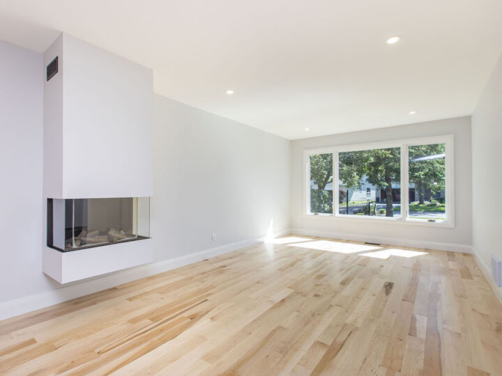 Bright living room with natural maple hardwood, a white wall-hung three-sided fireplace and a wide front window