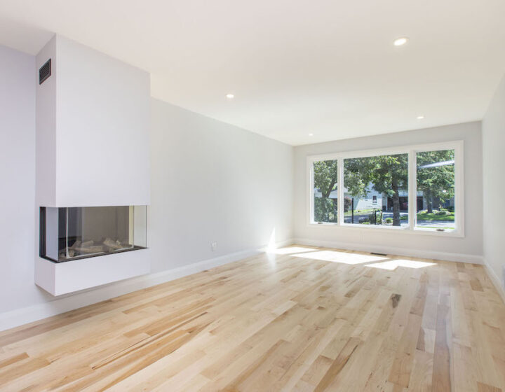 Bright living room with natural maple hardwood, a white wall-hung three-sided fireplace and a wide front window