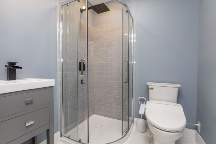 Small bathroom with a curved glass corner shower, grey wall tile, a grey vanity and a bidet toilet