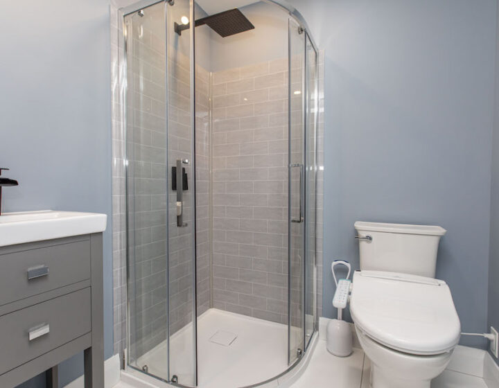 Small bathroom with a curved glass corner shower, grey wall tile, a grey vanity and a bidet toilet