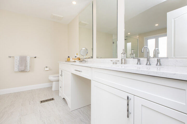 Long white vanity with a marble-look quartz top, two chrome faucets, a makeup counter and wall mirrors