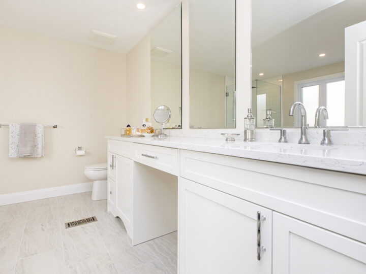 Long white vanity with a marble-look quartz top, two chrome faucets, a makeup counter and wall mirrors