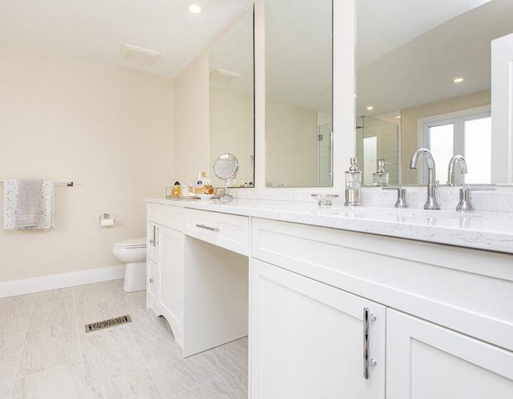 Long white vanity with a marble-look quartz top, two chrome faucets, a makeup counter and wall mirrors