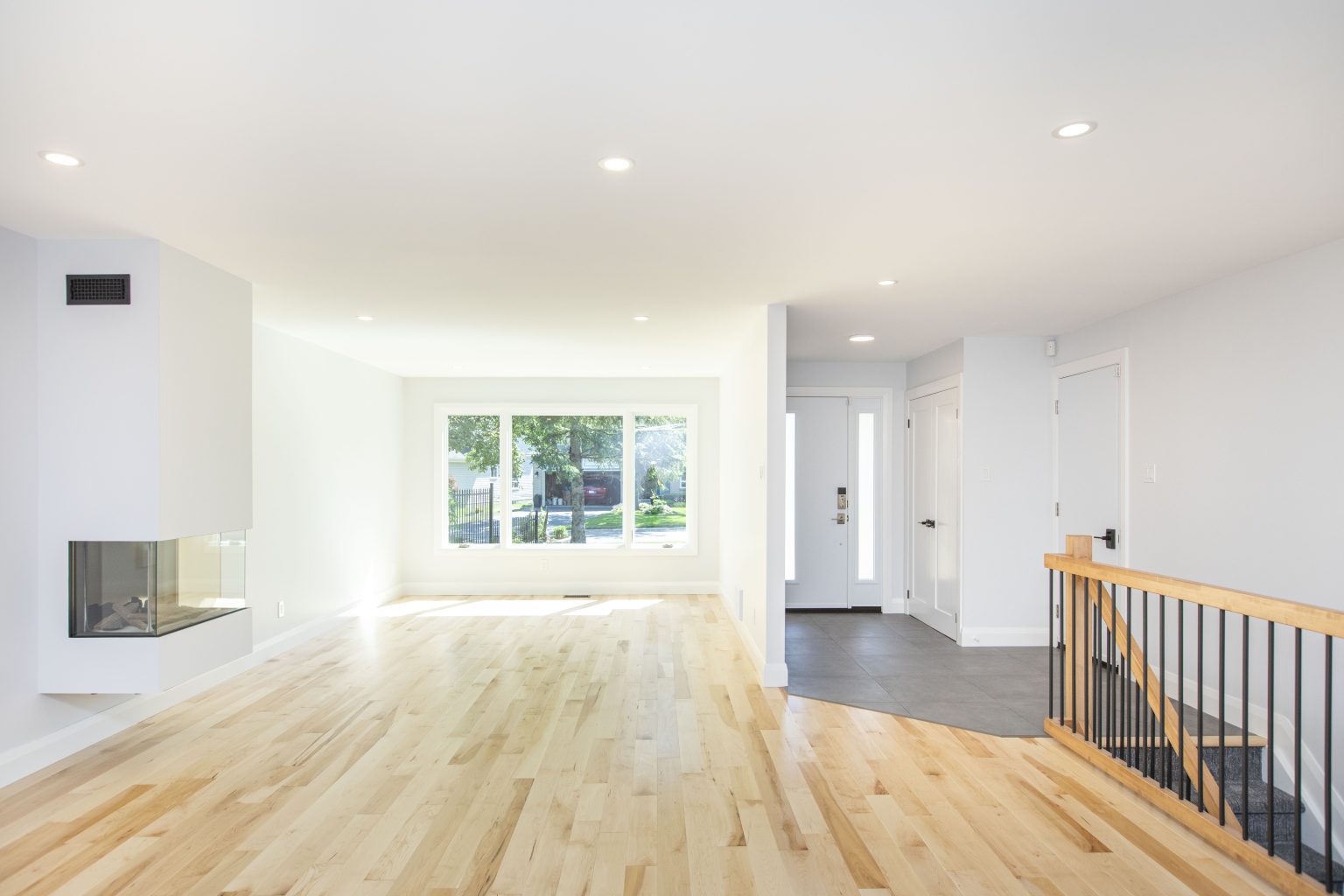 14 Living room with a new natural maple hardwood floor, a wall-hung corner fireplace, a tiled front entry and an oak stair railing with black spindles
