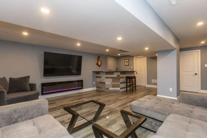 Finished basement family room with a sectional, a TV over a linear electric fireplace and a plank-clad bar