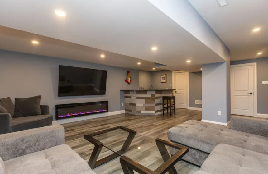 Finished basement family room with a sectional, a TV over a linear electric fireplace and a plank-clad bar