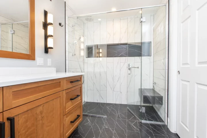Bathroom with a wood shaker vanity and a frameless glass walk-in shower with marble-look tile and a bench