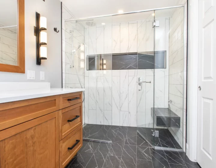 Bathroom with a wood shaker vanity and a frameless glass walk-in shower with marble-look tile and a bench