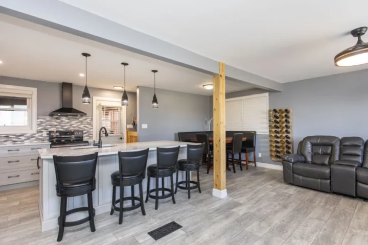 Open-concept main floor with a quartz island, black bar stools, a natural wood post and a leather sectional
