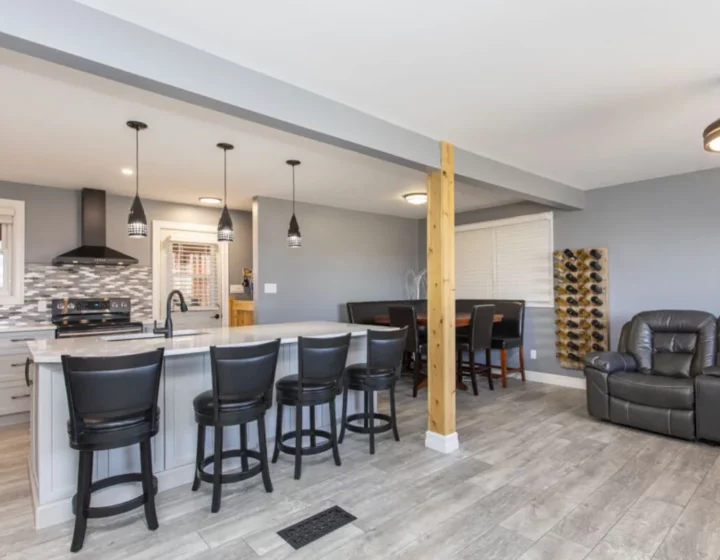Open-concept main floor with a quartz island, black bar stools, a natural wood post and a leather sectional