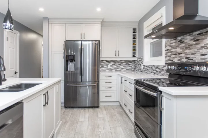 White shaker kitchen with a stainless French-door fridge, black range hood and grey mosaic backsplash