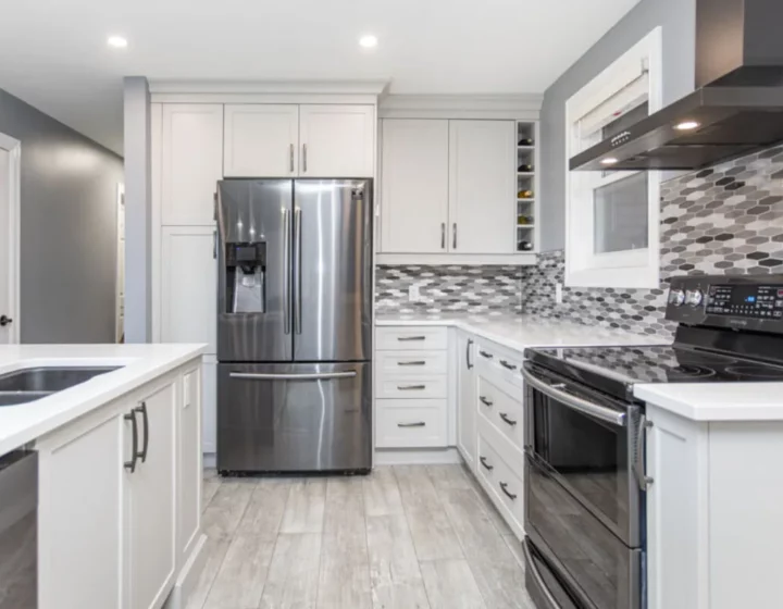 White shaker kitchen with a stainless French-door fridge, black range hood and grey mosaic backsplash