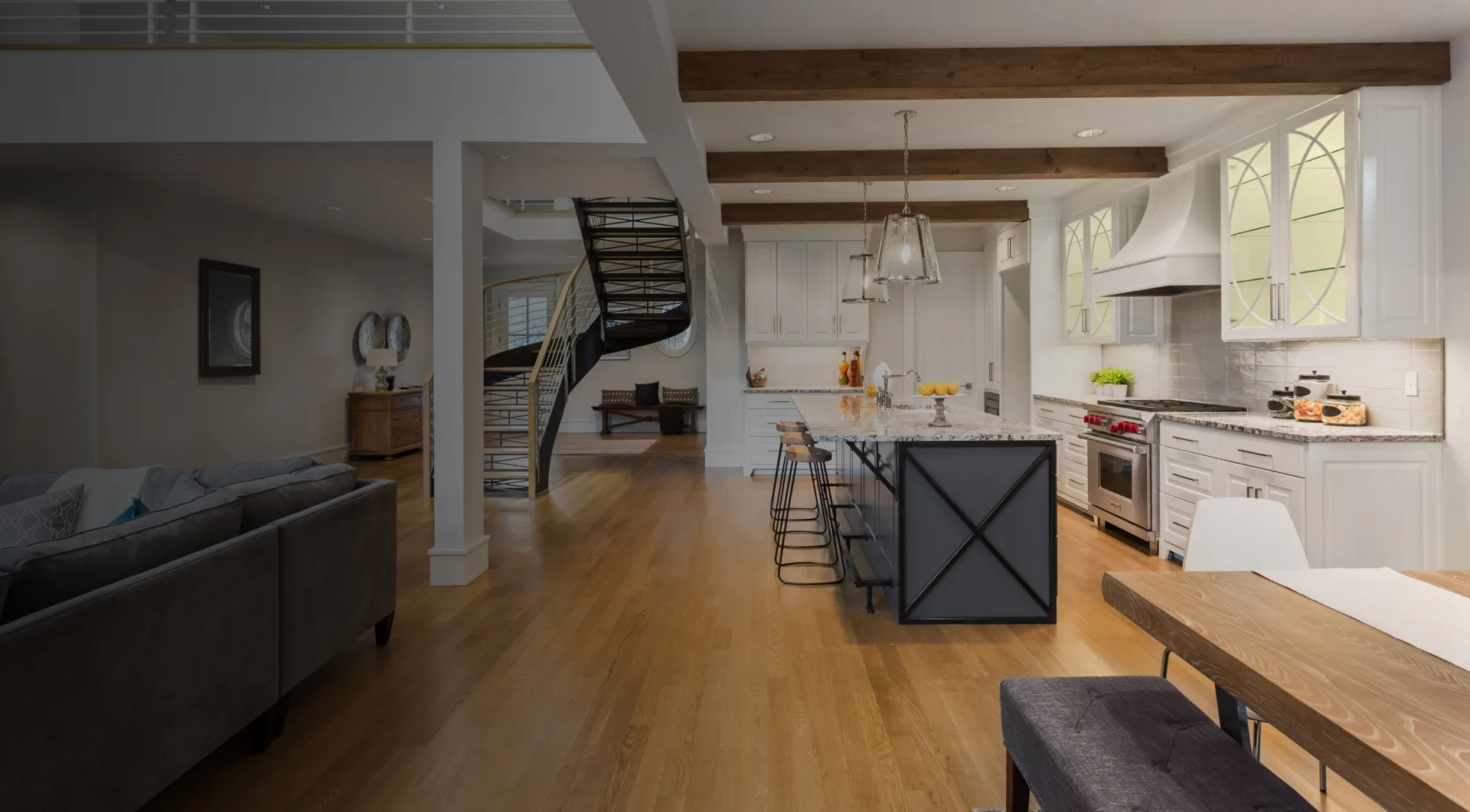 Open-plan kitchen with white cabinets, a dark island, light wood flooring and exposed timber beams.