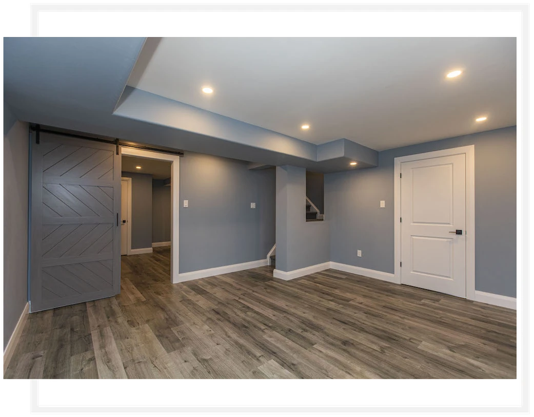 Finished basement with blue-grey walls, wood-look flooring and recessed ceiling lights.