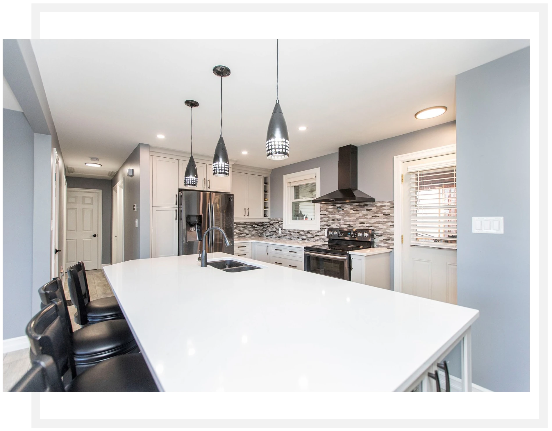 Kitchen with a long white island, black pendant lights and a grey tile backsplash.